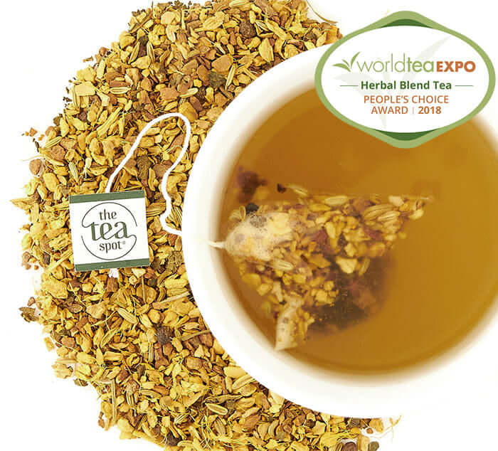 Cup of award-winning Turmeric Tonic loose leaf tea with herbal blend, showcasing The Tea Spot brand, surrounded by dry tea leaves.