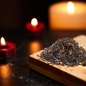 a pile of tea sits on a wooden board with candles in the background